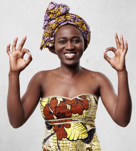 Everything is just fine! Beautiful cheerful African woman wearing bright scarf on head and elegant dress showing ok sign demonstrating her satisfaction and happiness agreeing with something.